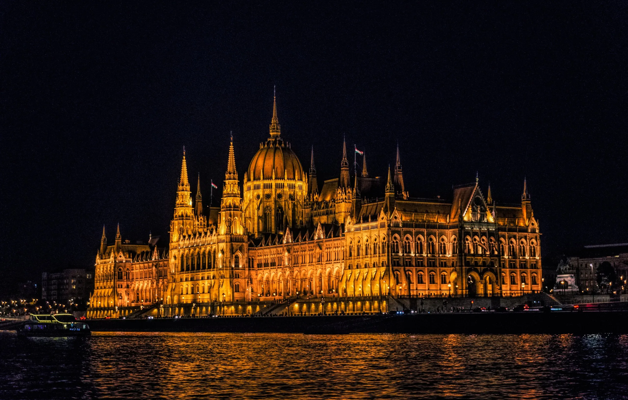 The Hungarian Parliament floodlit gold at night, seen across the dark water of the Danube.