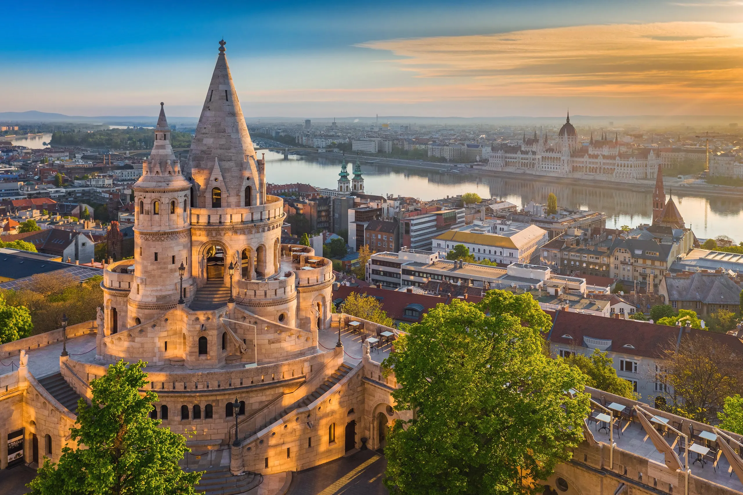 Fisherman's Bastion at sunrise, its white stone turrets above the Danube with the Parliament on the far bank.